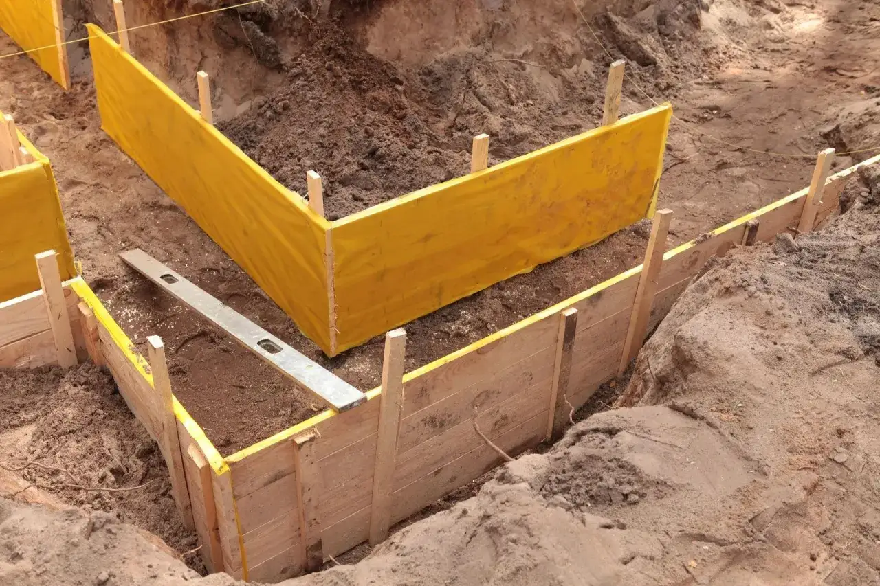 Wykonano wykopy pod fundamenty. Widać drewniane szalunki i żółtą folię.