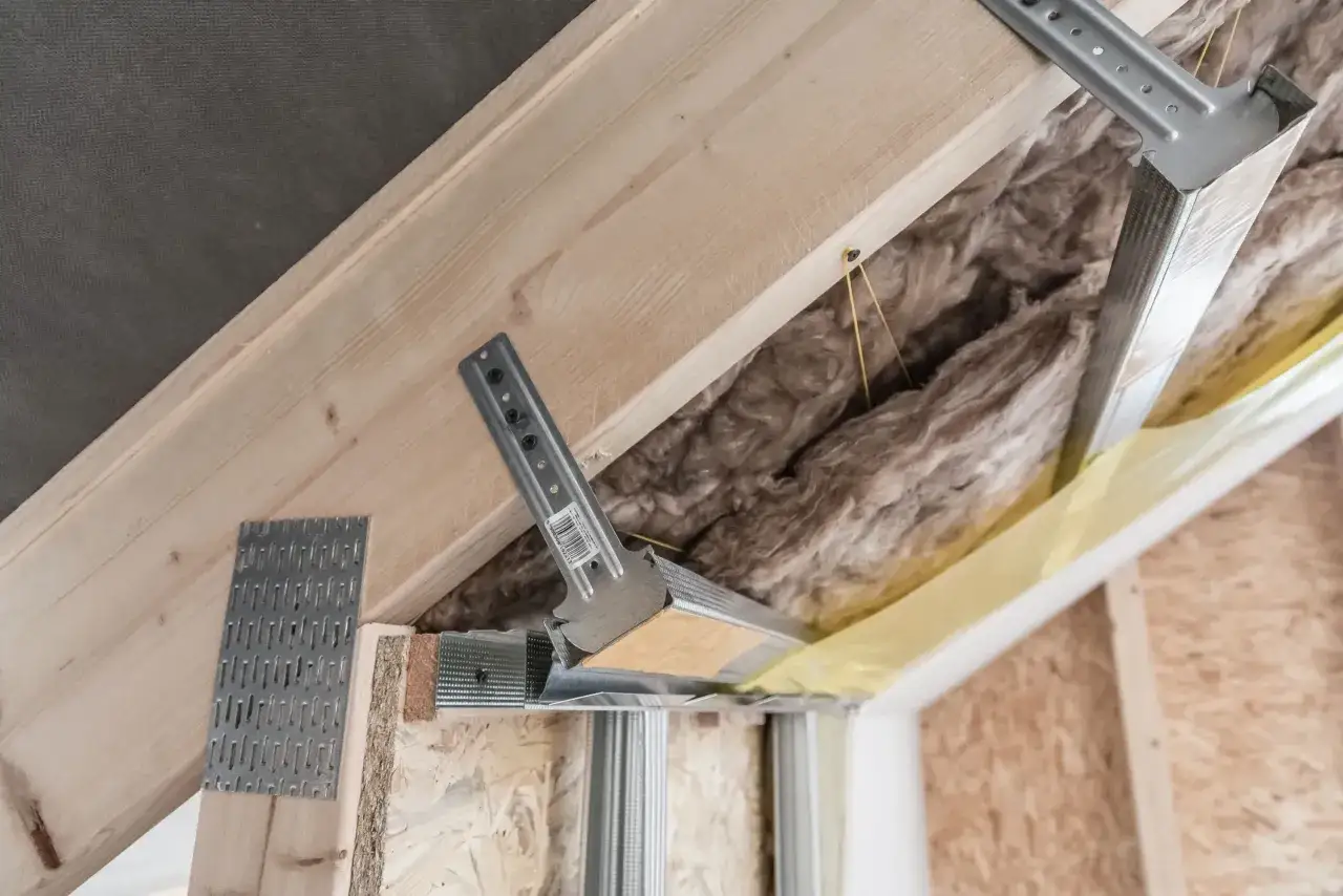 Konstrukcja podwieszanego sufitu z wełną mineralną. Widać metalowe profile i drewniane elementy, a także mocowania. Pytanie: jakie wkręty do wieszaków grzybkowych?