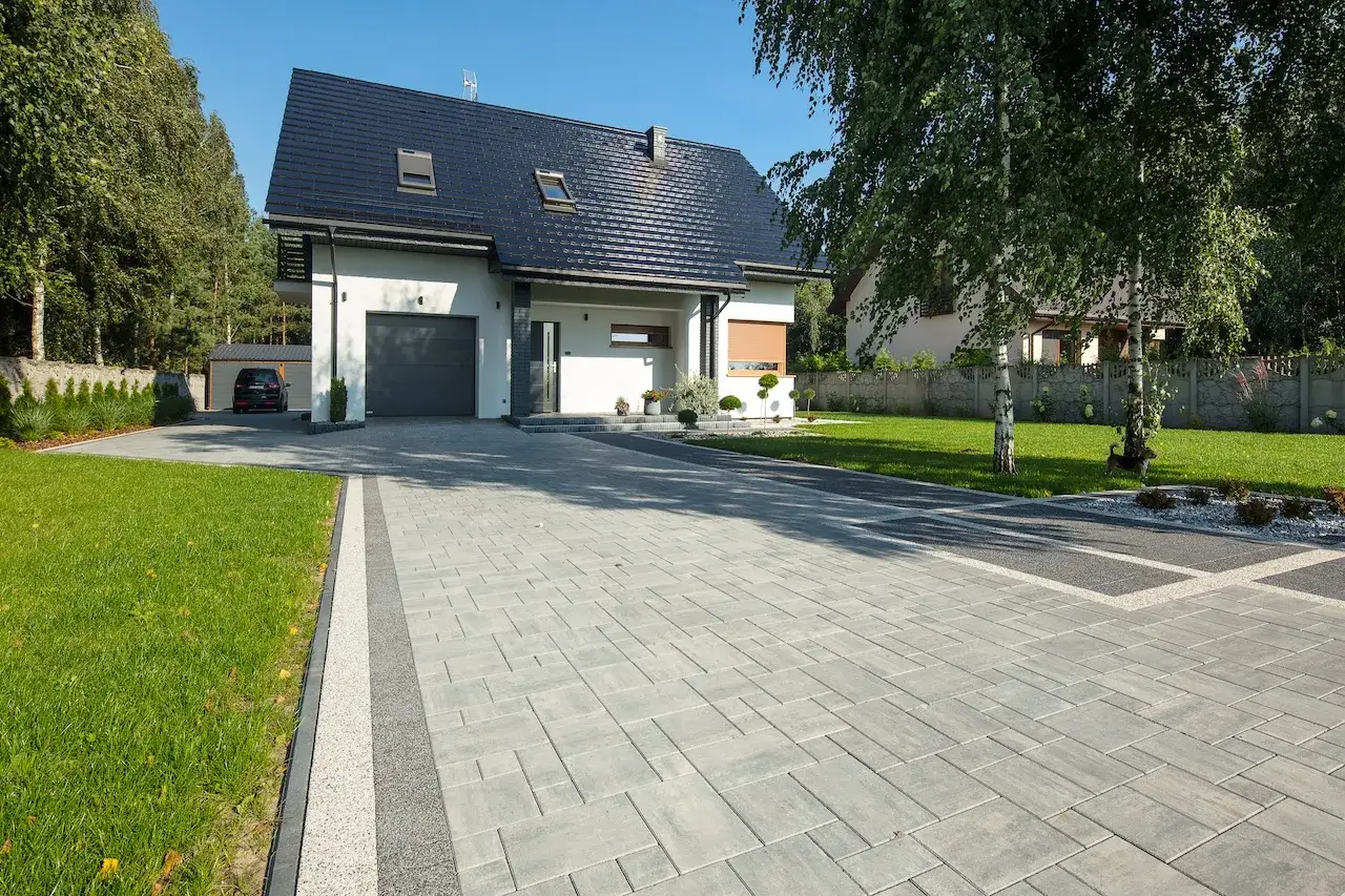 Nowoczesny podjazd z szarej kostki brukowej, elegancka alternatywa co zamiast kostki na podjazd. Dom z garażem, zadbany ogród.