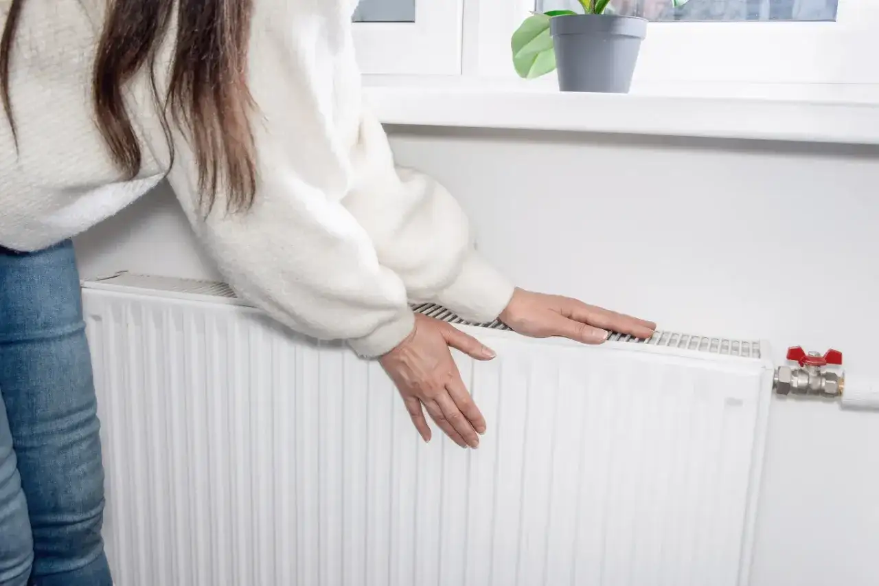 Kobieta sprawdza temperaturę grzejnika, przygotowując się na sezon grzewczy. Kiedy zaczyna się sezon grzewczy? Zazwyczaj od października do kwietnia.