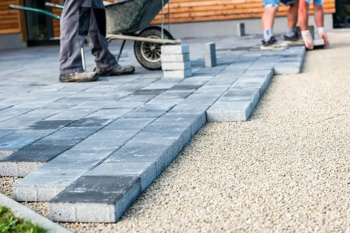 Układanie płyt betonowych na podjeździe – alternatywa dla kostki. Pracownicy budowlani tworzą nową nawierzchnię.