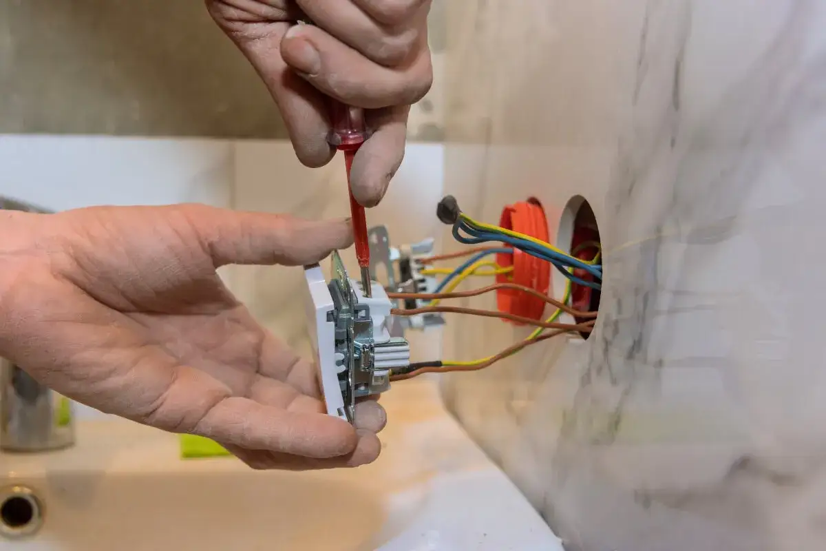 Elektryk montuje gniazdko, zastanawiając się, ile za punkt elektryczny. Widać przewody i puszkę instalacyjną.