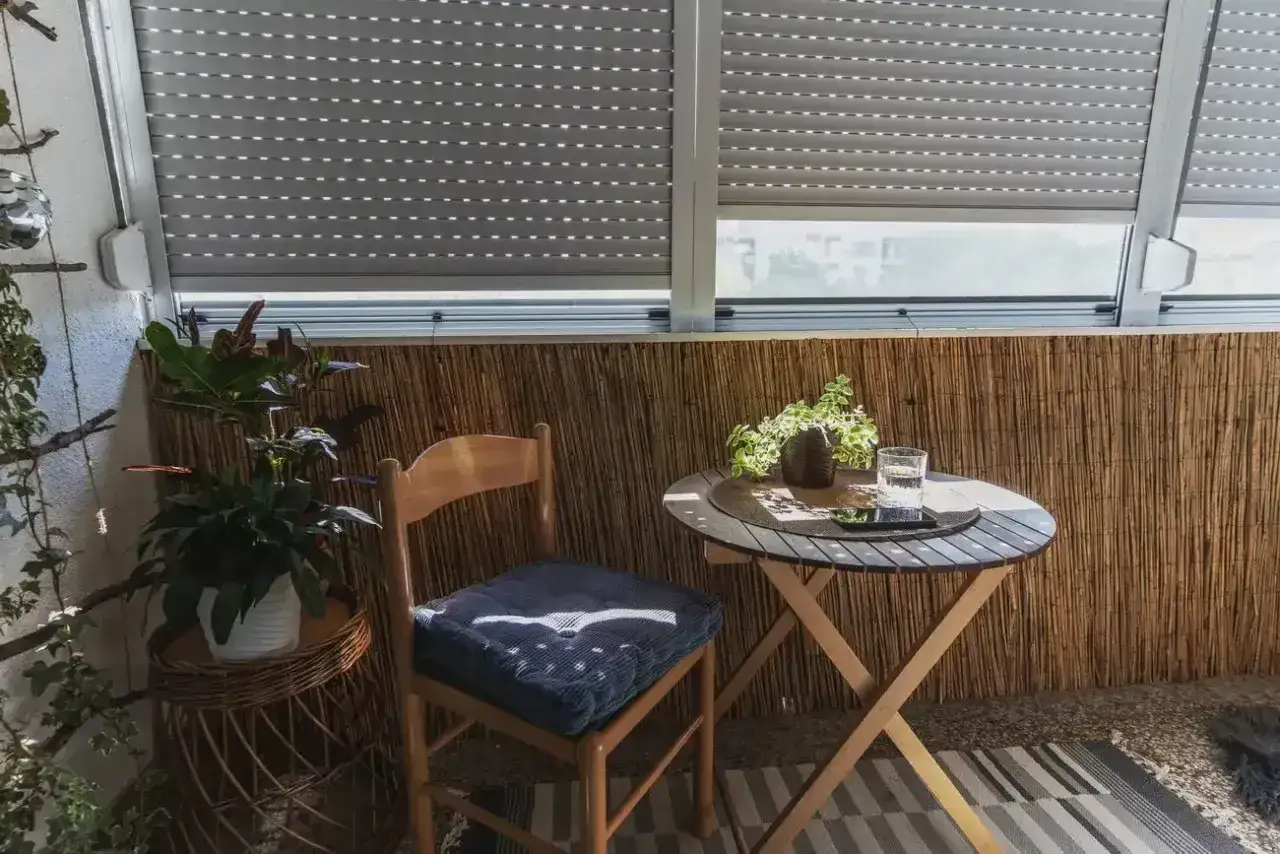 Przytulna loggia z bambusową ścianką, drewnianym krzesłem i stolikiem. Idealne miejsce na poranną kawę na balkonie.