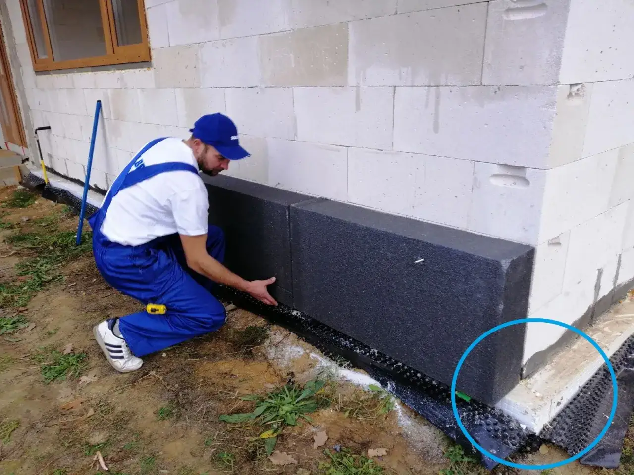 Pracownik montuje styropian na fundamencie, by zapobiec zimno w domu po ociepleniu.