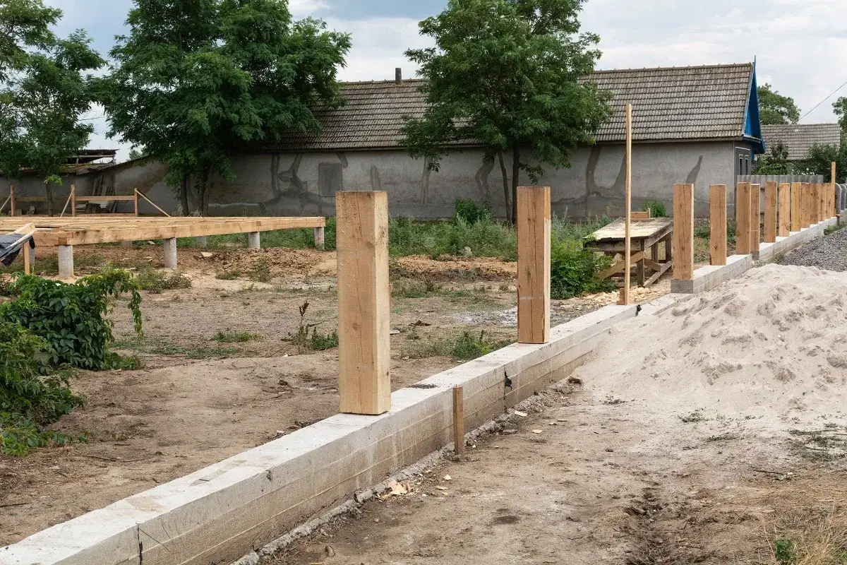 Budowa domu w toku. Zastanawiasz się, ile bierze geodeta za wytyczenie działki? Na placu budowy widać fundamenty, drewniane słupy i przygotowania do dalszych prac.